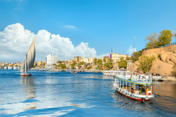 Sailboat and traditional felucca on the Nile River in Egypt with a scenic city backdrop.