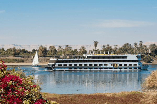 Luxury Nile cruise boat sailing on the Nile River in Egypt with a traditional felucca in the background.