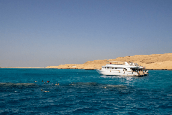 Yacht with snorkelers in clear blue water near arid coast.