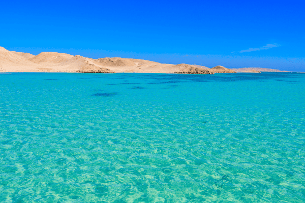 Crystal-clear turquoise sea by arid desert landscape.