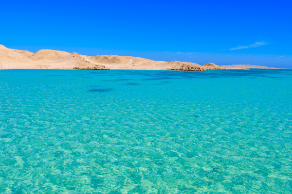 Crystal-clear turquoise sea by arid desert landscape.