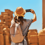 Traveler, traveling with Discovery Tours Egypt, taking a photo of ancient ruins in Egypt with a smartphone, wearing a straw hat, capturing Egypt’s rich history.