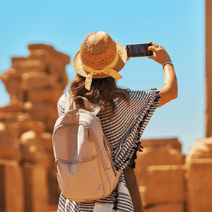 Traveler, traveling with Discovery Tours Egypt, taking a photo of ancient ruins in Egypt with a smartphone, wearing a straw hat, capturing Egypt’s rich history.