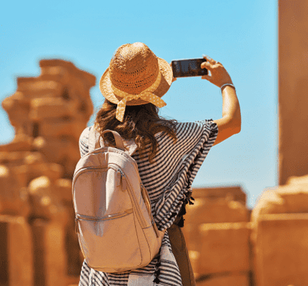 Traveler, traveling with Discovery Tours Egypt, taking a photo of ancient ruins in Egypt with a smartphone, wearing a straw hat, capturing Egypt’s rich history.