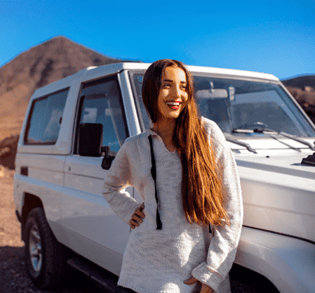 Smiling traveler standing next to a 4x4 vehicle in the desert of Egypt with mountains in the background.