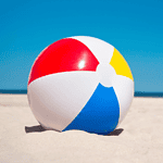 Colorful beach ball resting on sandy beach in Egypt with ocean and clear blue sky in the background.