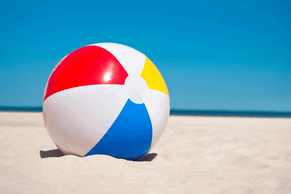 Colorful beach ball resting on sandy beach in Egypt with ocean and clear blue sky in the background.