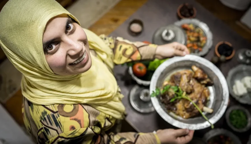 Woman presenting traditional dish, smiling in kitchen.