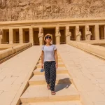 Visitor walking towards the Hatshepsut Temple in Egypt with ancient statues in the background.