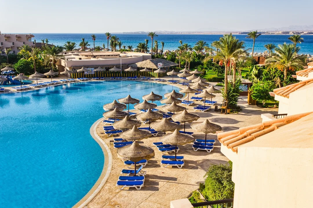 Beautiful resort pool area with beach umbrellas and sun loungers overlooking the Red Sea in Egypt.
