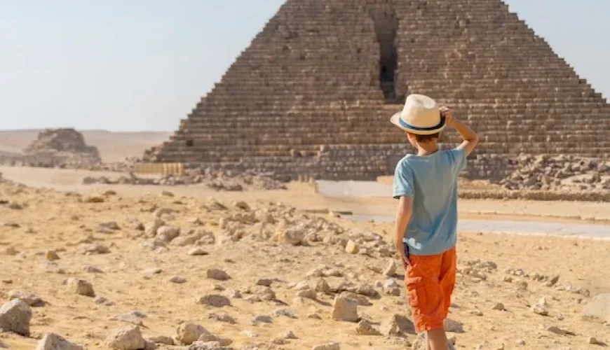 Child observing the Great Pyramid of Giza in Egypt while standing on the sandy desert.