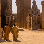 Two men walking among ancient Egyptian temple ruins.