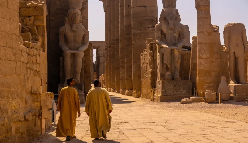 Two men walking among ancient Egyptian temple ruins.
