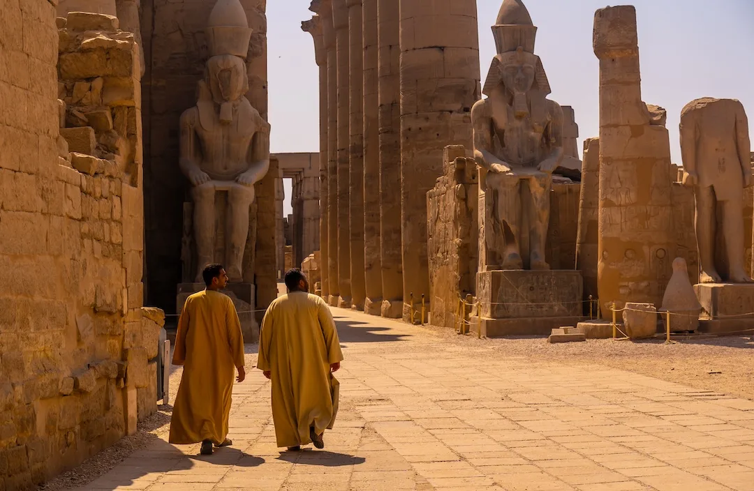 Two men walking among ancient Egyptian temple ruins.