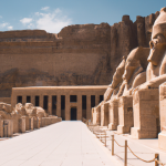 Ancient Egyptian temple with colossal statues under blue sky.