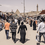 Bustling outdoor market near ancient pyramid and minaret.