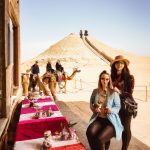 Tourists on camel ride near desert pyramids.