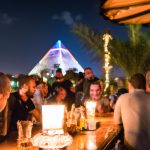People socialising at night with lit pyramid in background.