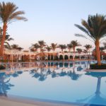 Tropical resort pool with palm tree reflections at sunset.