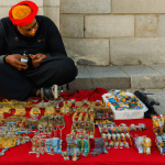 Street vendor selling colorful crafts on a red cloth.